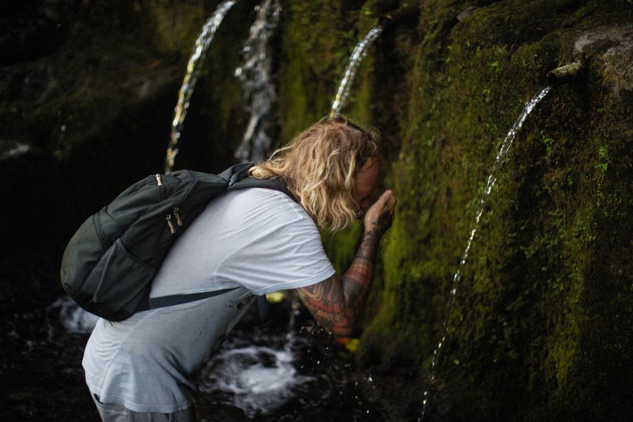 hombre tatuado bebiendo cascada natural 2 Hombre tatuado bebiendo en cascada natural